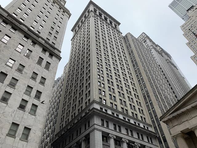 Looking up at tall, historic buildings with many windows in the Wall Street area.