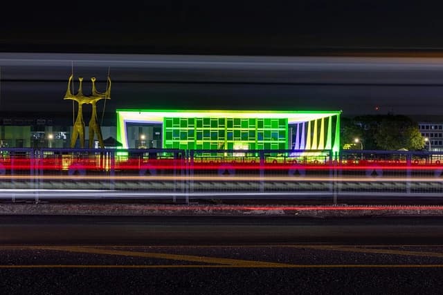 Supreme Federal Court building in Brazil, illuminated green at night, with light trails from passing vehicles.