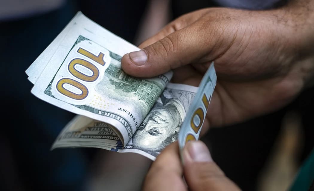 A person's hands holding several United States one-hundred-dollar bills.