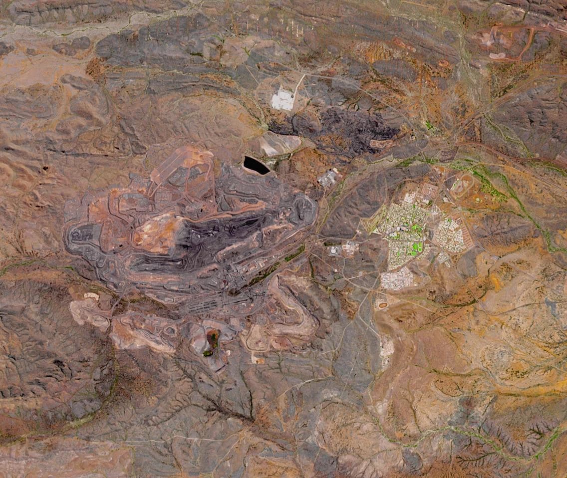 Aerial view of a vast open-pit iron ore mine in a rugged landscape.