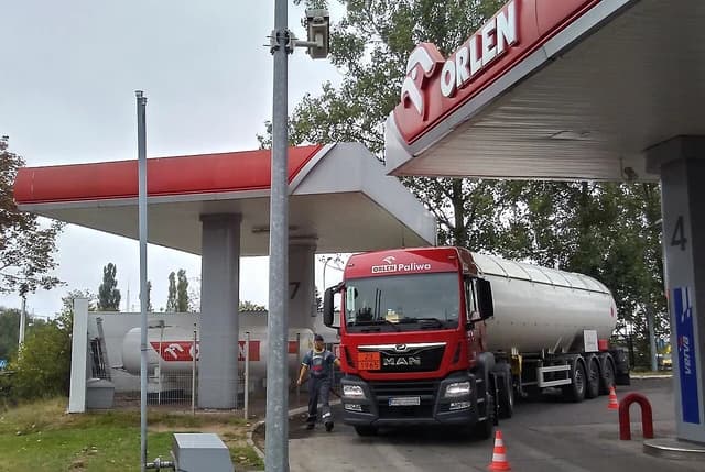 A red fuel delivery truck with a white tanker trailer parked at an Orlen gas station.