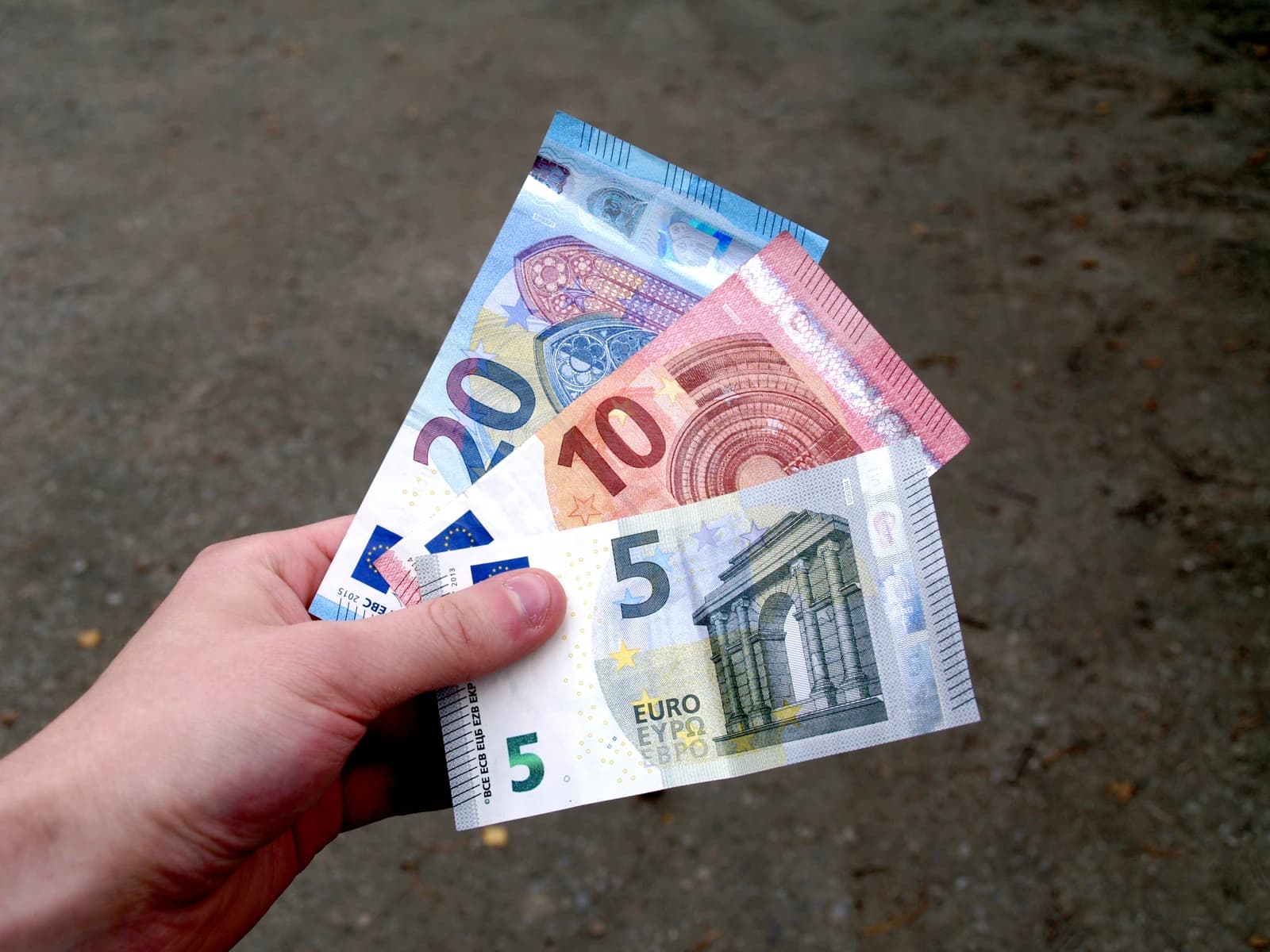 Person's hand holding five, ten, and twenty euro banknotes.