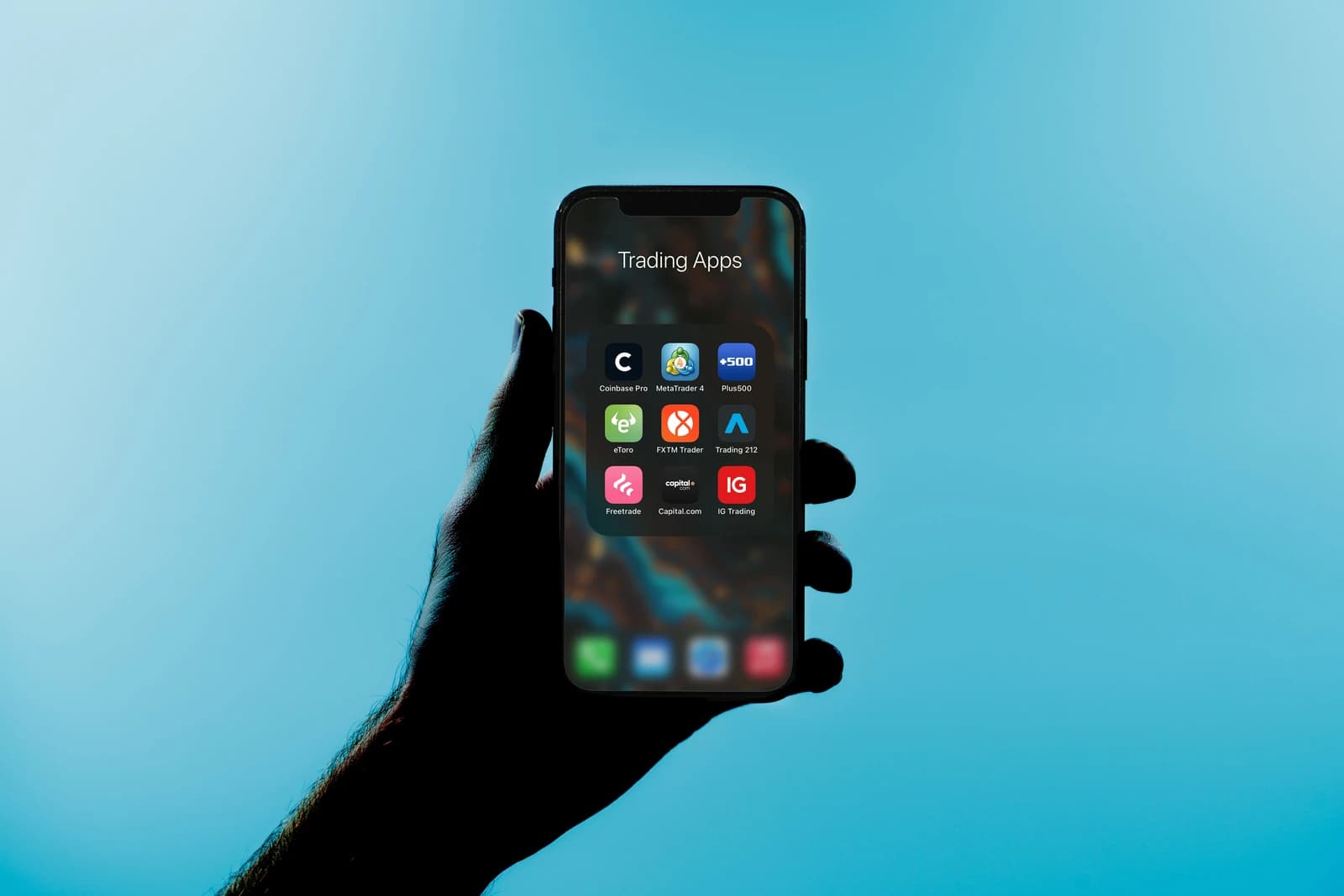 Hand holding an iPhone with financial trading app icons on the screen.