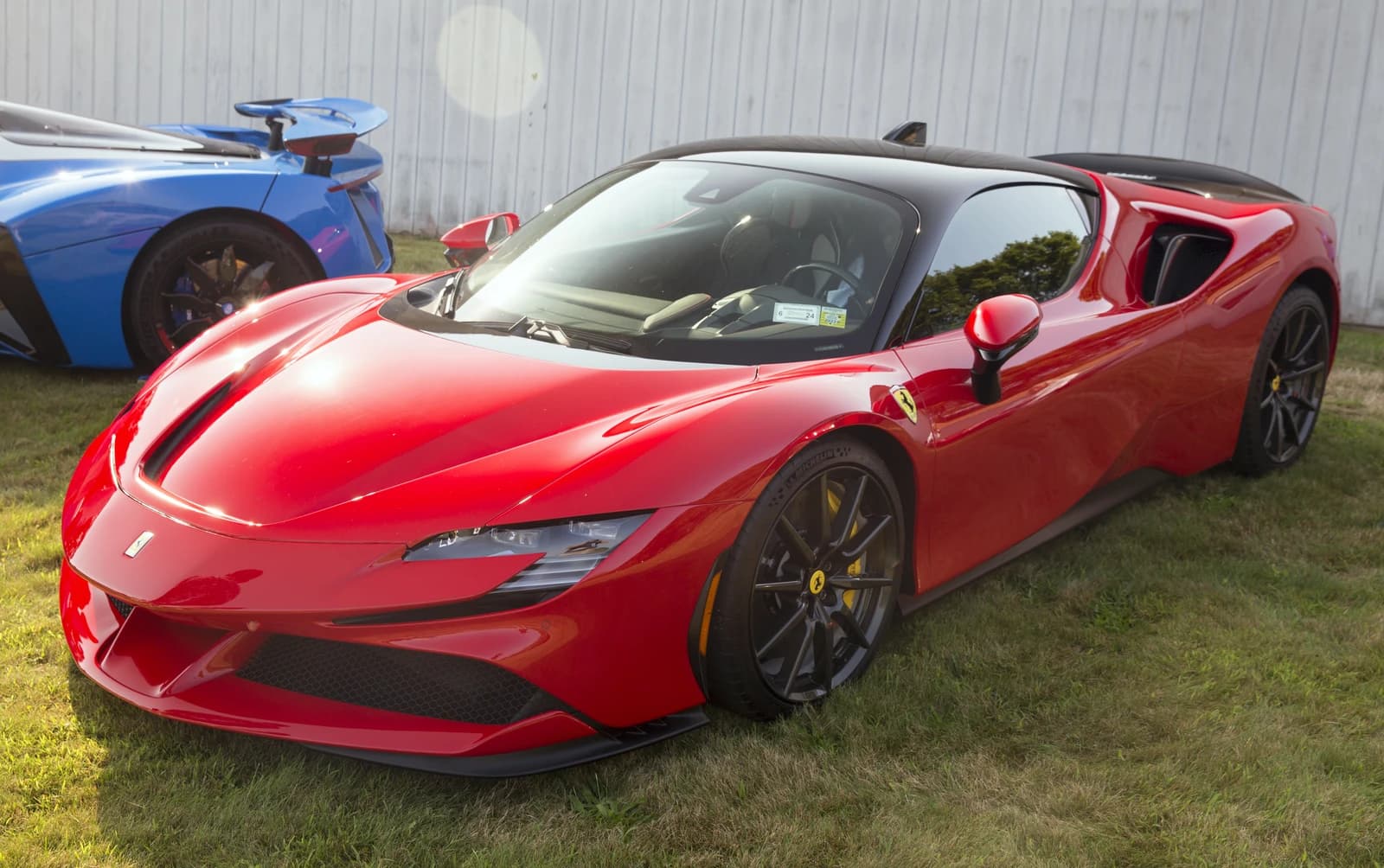 Red Ferrari SF90 Stradale sports car parked on grass at an outdoor event.
