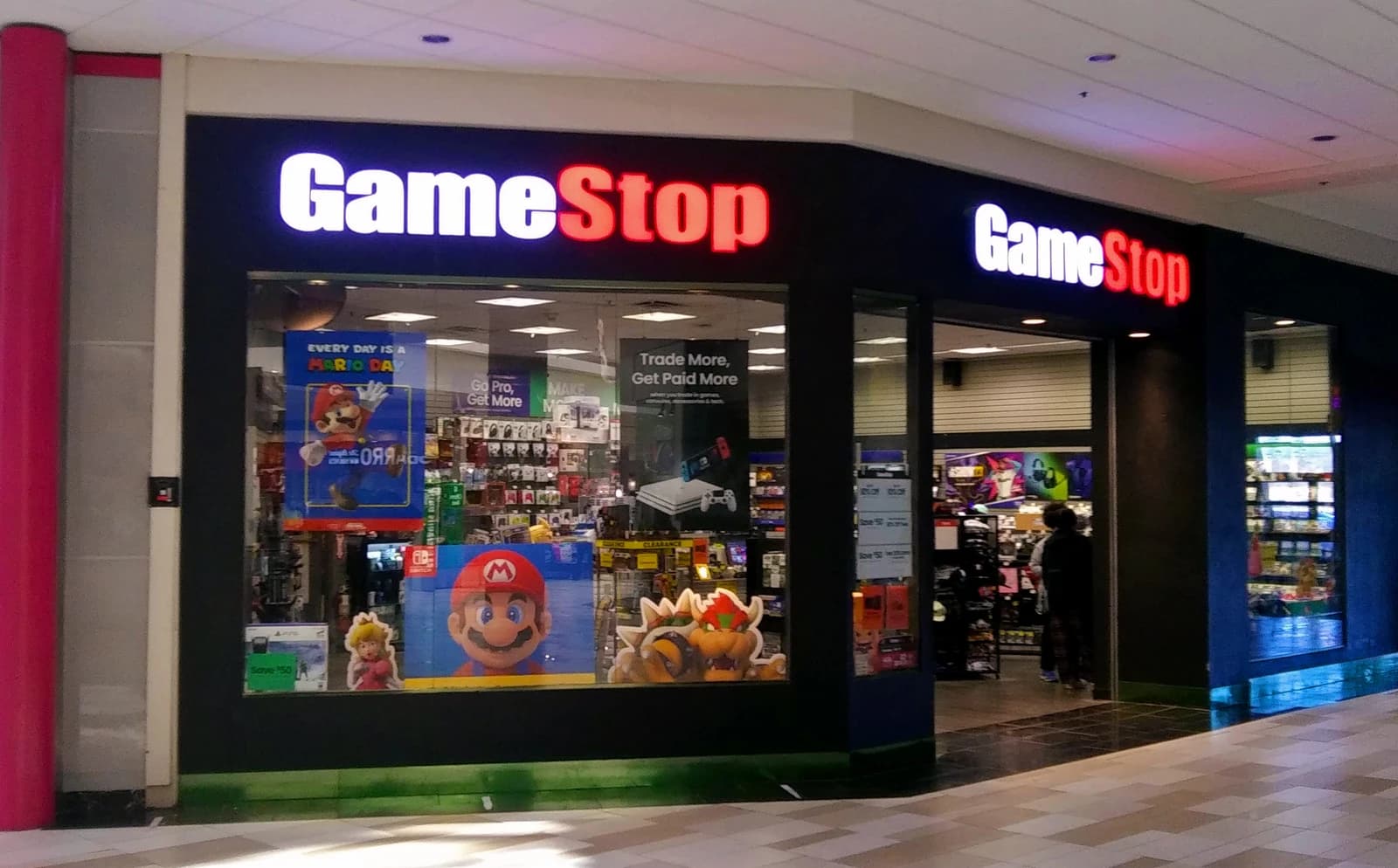 GameStop storefront with its illuminated sign and promotional posters for video games.