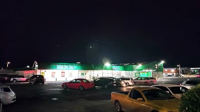 Exterior view of Woolworths Mornington supermarket illuminated at night with cars parked outside.