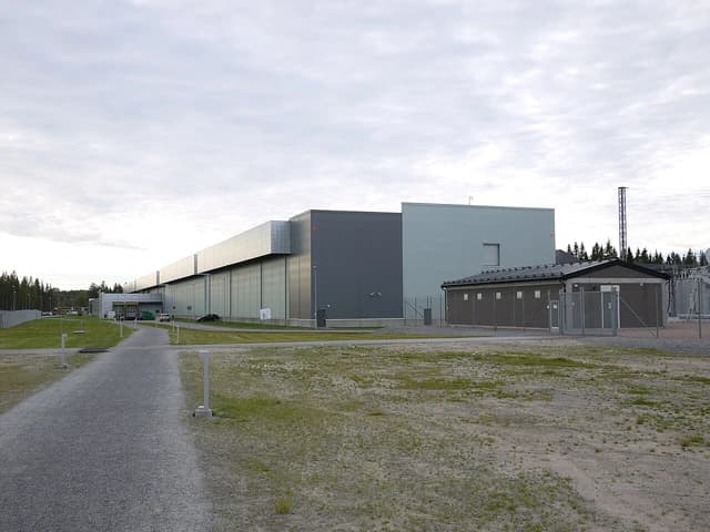 Exterior view of a large, modern data center building with a gravel path leading towards it.