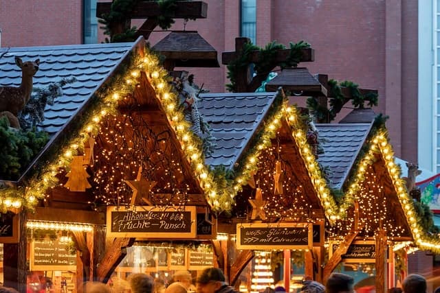 Christmas market stalls decorated with lights and garlands, with people visible at the bottom.