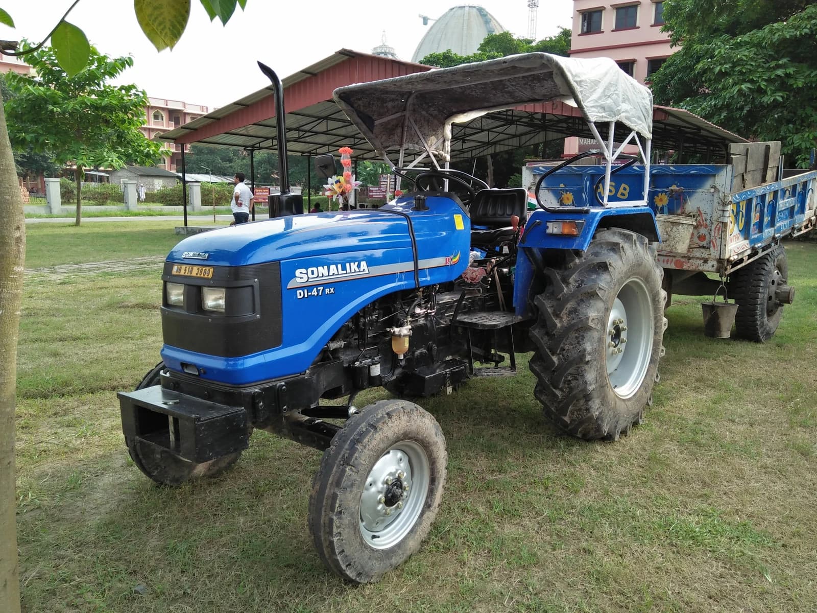 Sonalika D1-47 RX tractor in blue, with an attached carriage, parked on a grassy area.