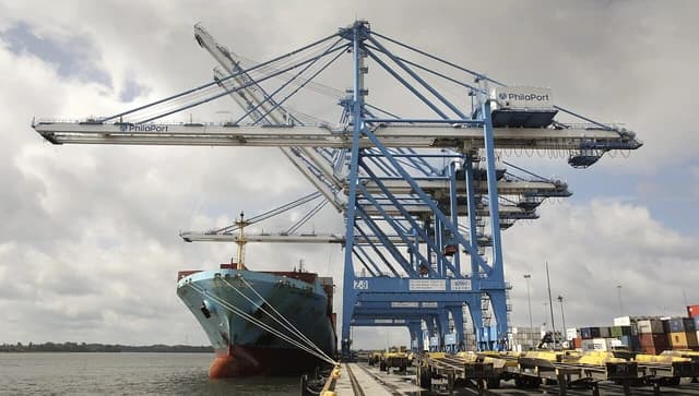 Container ship moored at a terminal with large cranes and stacks of containers.