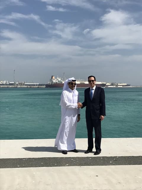 Steven Mnuchin and Saad Sherida Al-Kaabi shaking hands with ships in background.