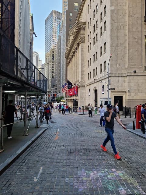People walking on a cobblestone street in front of the New York Stock Exchange building.