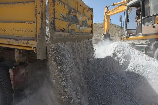 A dump truck unloads gravel at a construction site with an excavator nearby.