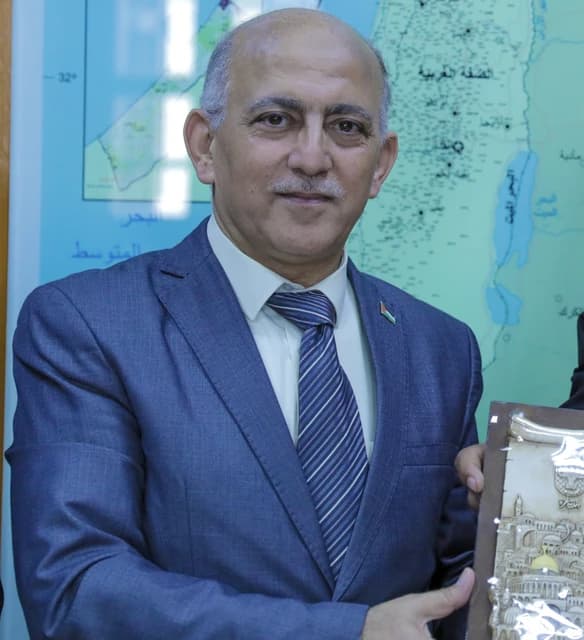 Gaza City Mayor Yahya Al-Farraj stands in his office holding a decorative plaque.
