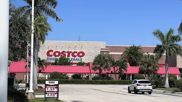 Exterior of a Costco Wholesale store with palm trees and a gasoline price sign.