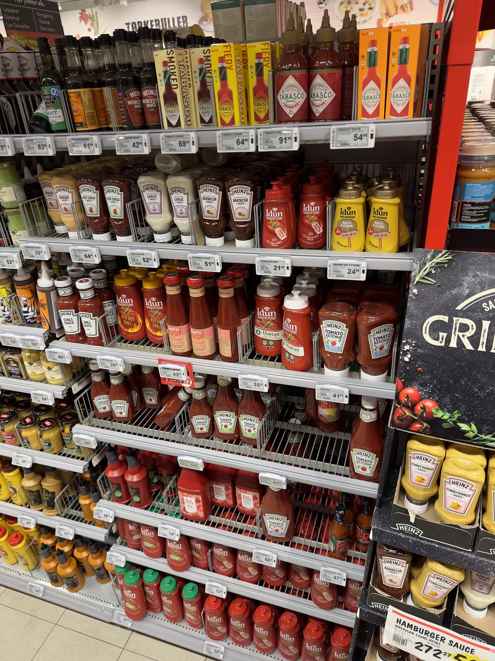 Supermarket aisle shelves filled with bottles of mustard, ketchup, and chili sauce.