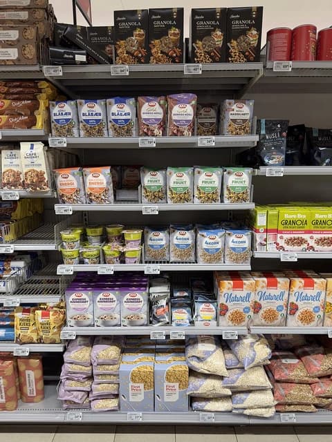 Supermarket aisle shelves displaying various brands of breakfast cereals and packaged food products.