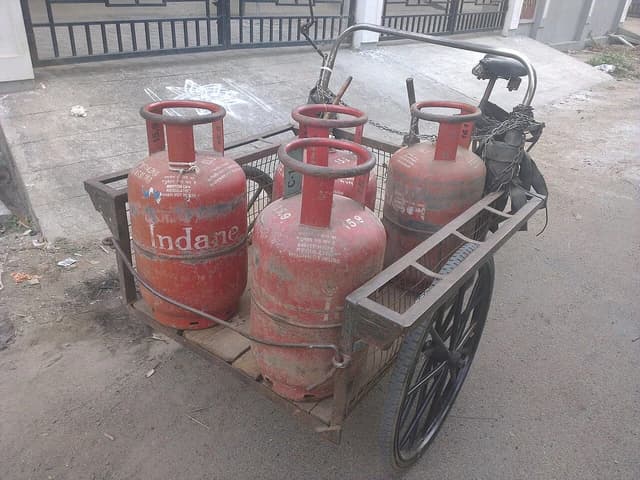 Several red Indane brand LPG gas cylinders loaded on a pushcart on a street.