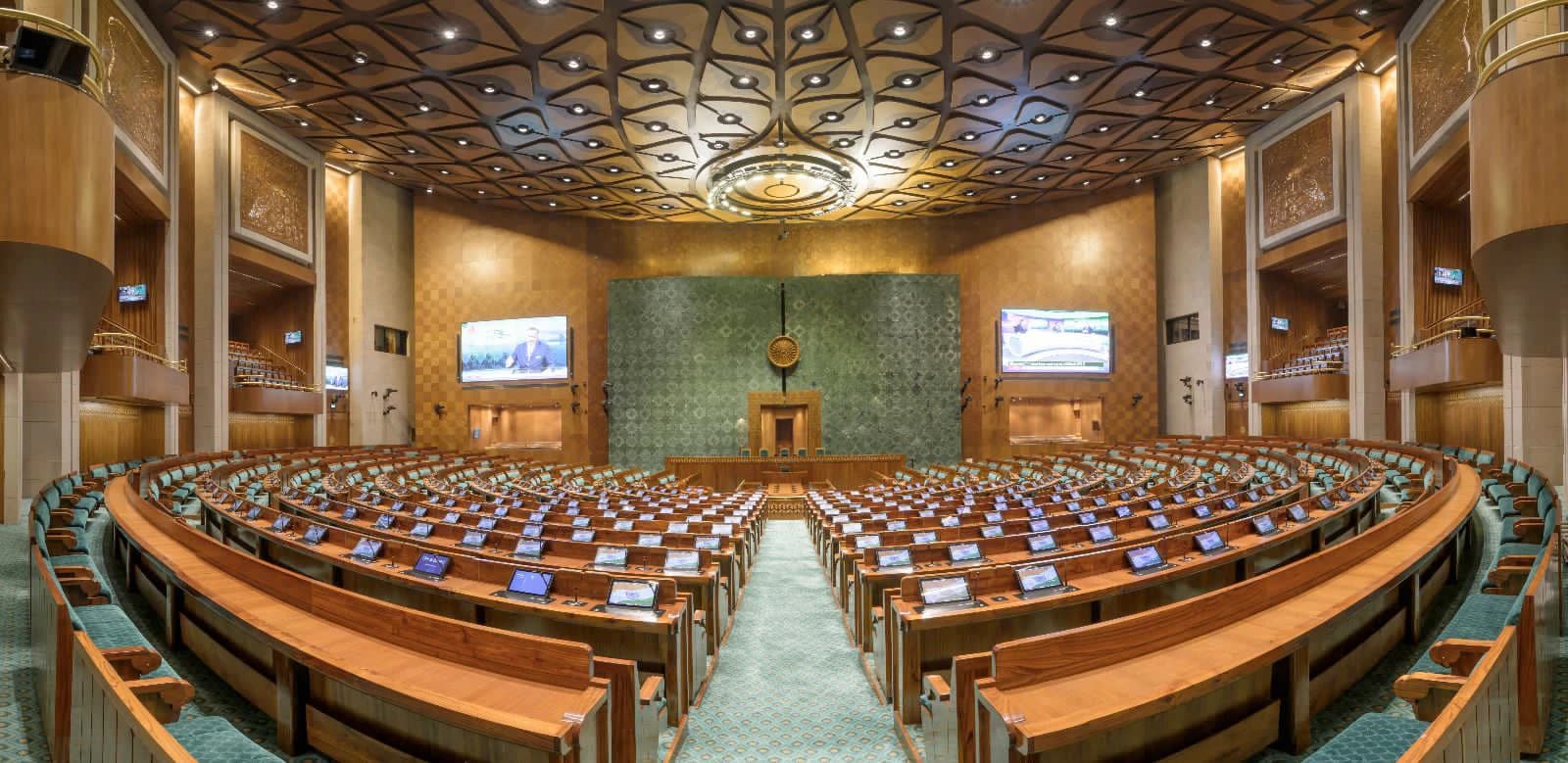 Empty Lok Sabha chamber in the New Parliament building with rows of seats and digital screens.