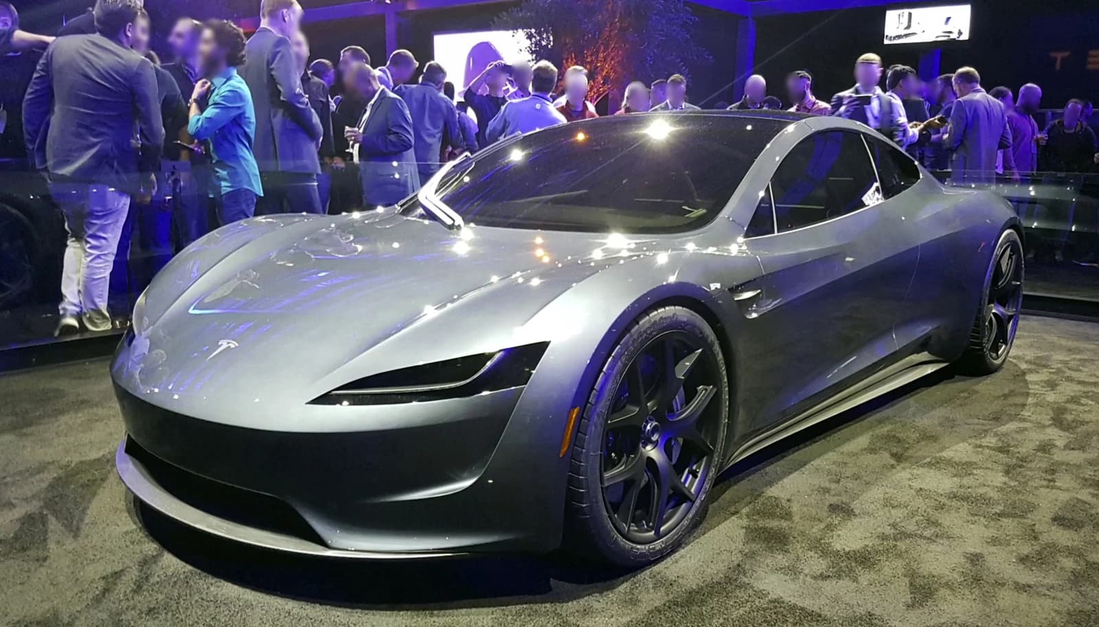 Gray Tesla Roadster prototype on display at a public event with people in the background.