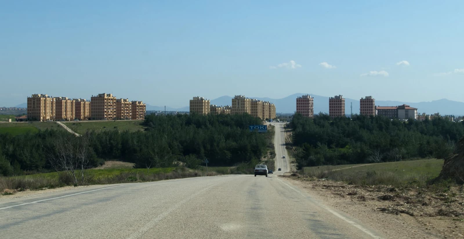 TOKİ residential buildings in Sarıçam, Adana, seen from a distance along a road.