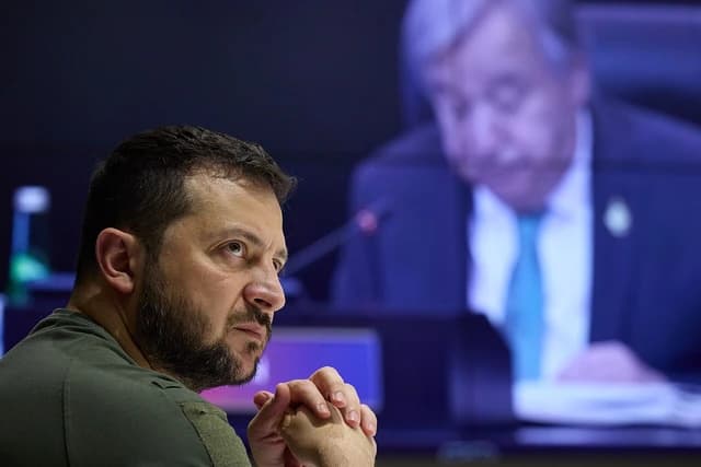 Volodymyr Zelenskyy, President of Ukraine, with hands clasped, looking intently to the side.