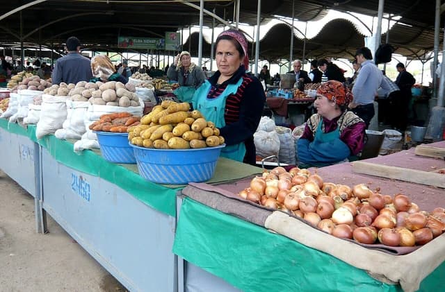 Woman vendor standing behind a display of potatoes and carrots at a market.