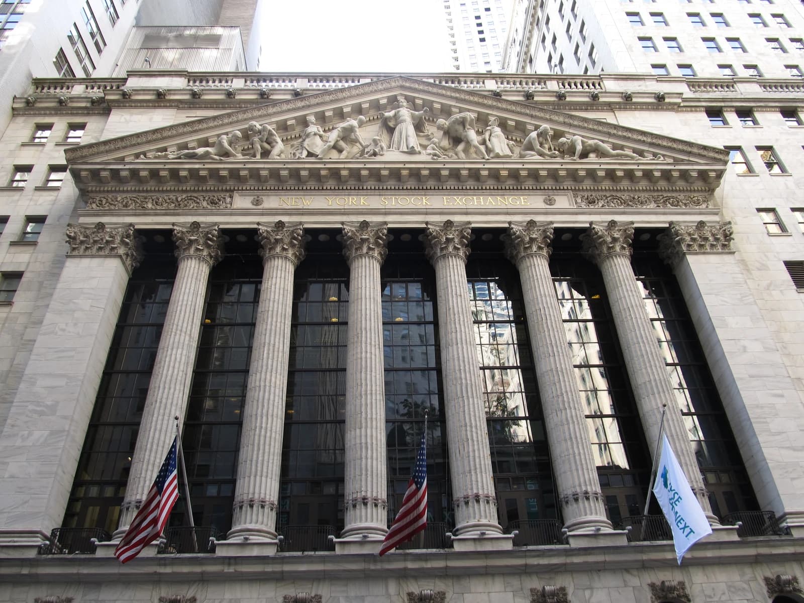 Exterior facade of the New York Stock Exchange with American flags and NYSE Group flag.