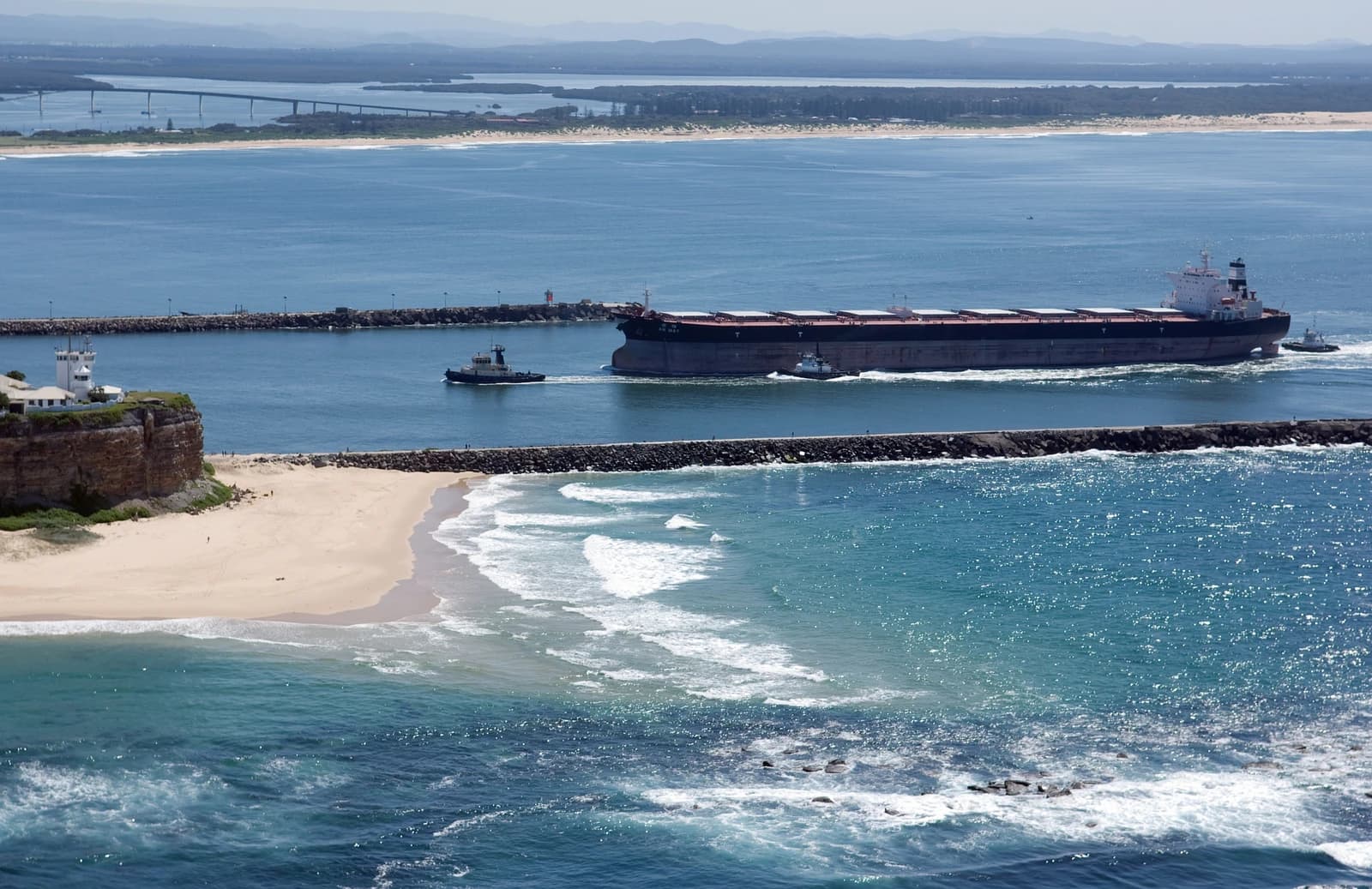 A large bulk carrier ship, escorted by two tugboats, enters Port Hunter.