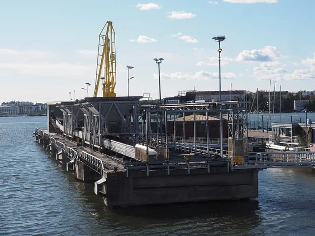A coal unloading facility with conveyor belts and a large yellow crane situated on a body of water.